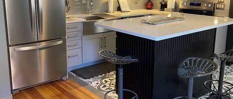 A modern kitchen with stainless steel appliances, a central island with stools, and a patterned floor.