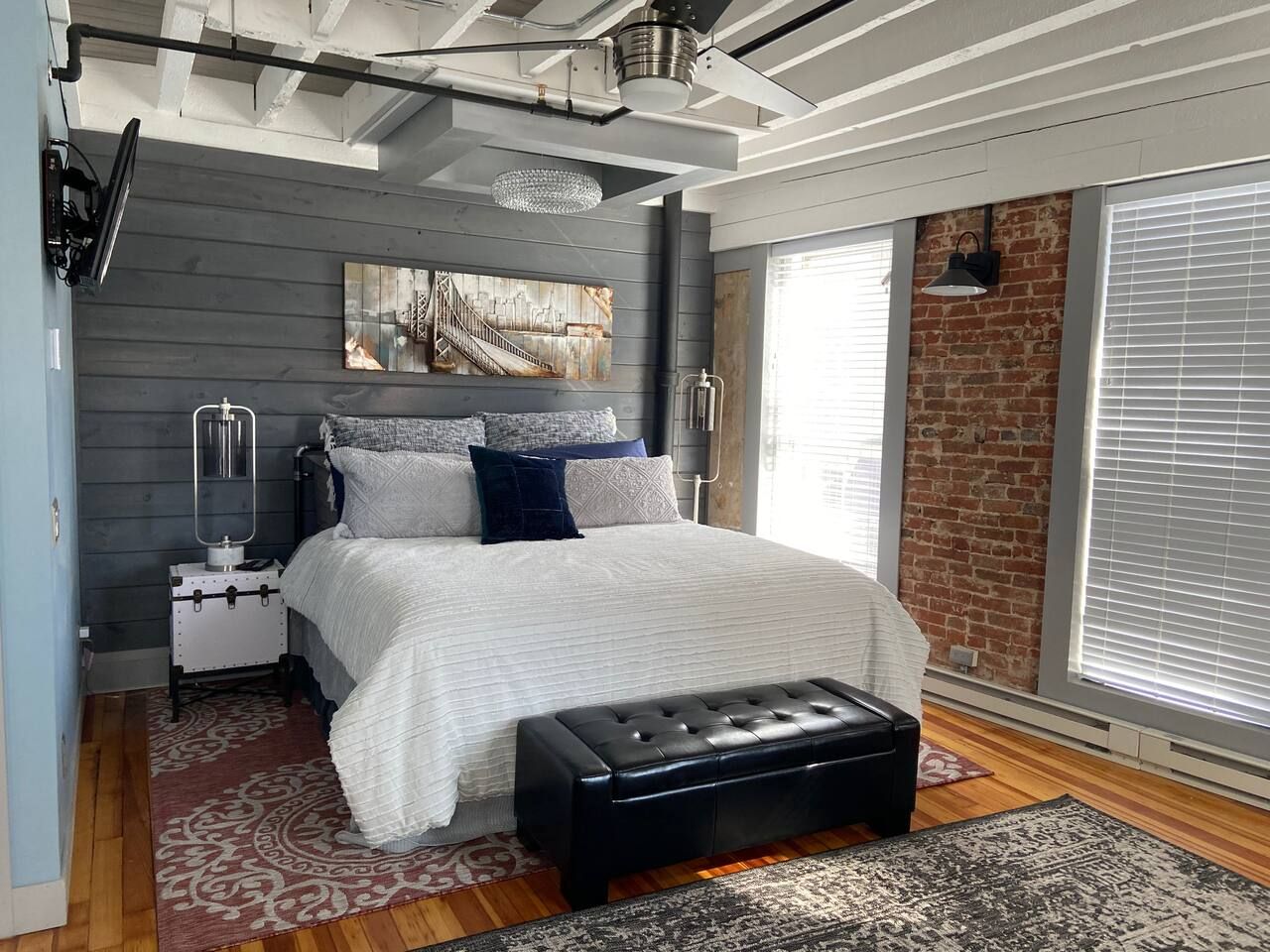 A modern bedroom with a large bed, a chest of drawers, a bench, and a cityscape painting on the wall.