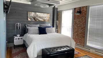 Un dormitorio moderno con una cama grande, un aparador, un banco y una pintura de un paisaje urbano en la pared.