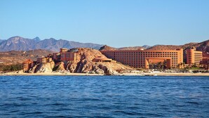 Um hotel à beira-mar com vários edifícios, uma praia e montanhas ao fundo.