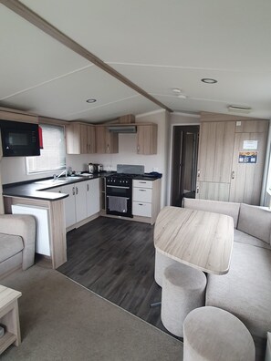 A compact RV kitchen with a stove, sink, and microwave, and a small dining area with a table and chairs. - Cabin Sleeps 6 With Hot Tub (Malton)