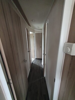 Un pasillo estrecho con puertas de madera y una pared blanca.