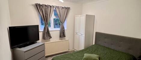 A bedroom with a bed, a television, a wardrobe, and a window with curtains.