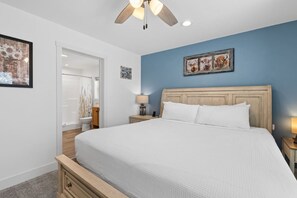 Ein Schlafzimmer mit einem Bett, einem Nachttisch, einer Lampe, einem Deckenventilator und Kunstwerken an der Wand.