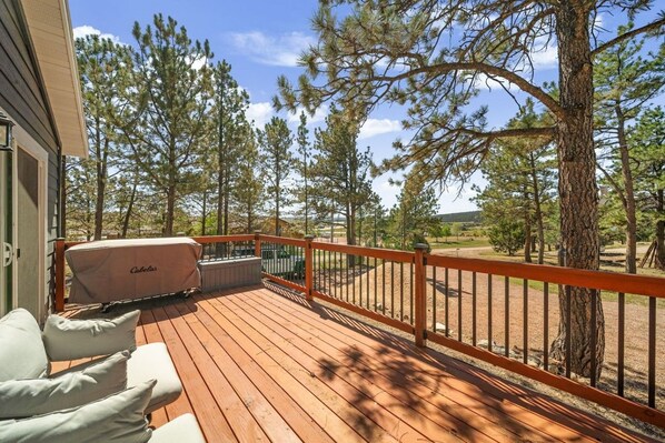 Eine Holzterrasse mit Gartenmöbeln, einem überdachten Grill und Blick auf ein bewaldetes Gebiet.