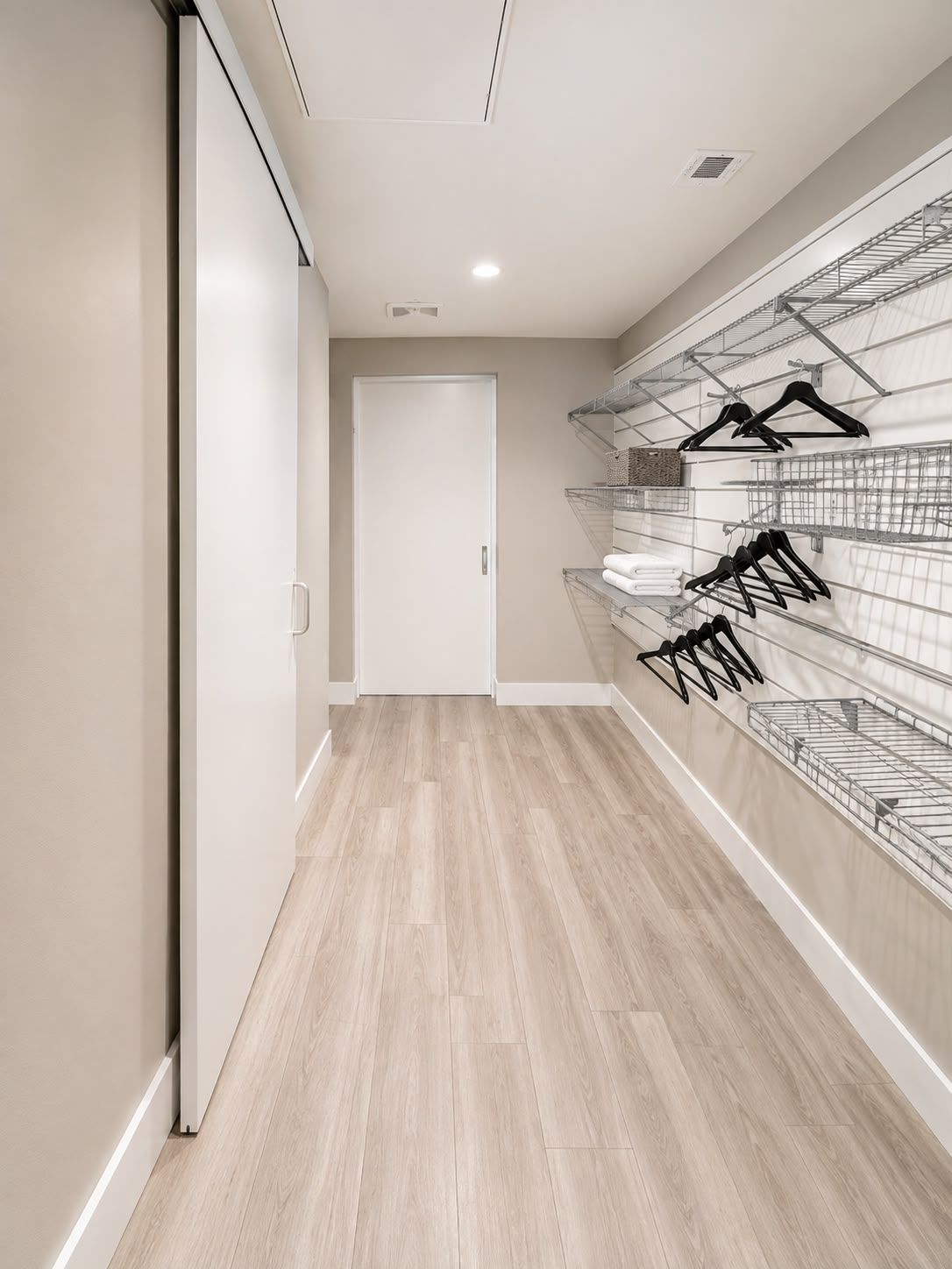 Un couloir avec une porte blanche au fond, un plancher en bois et des étagères métalliques équipées de porte-manteaux.