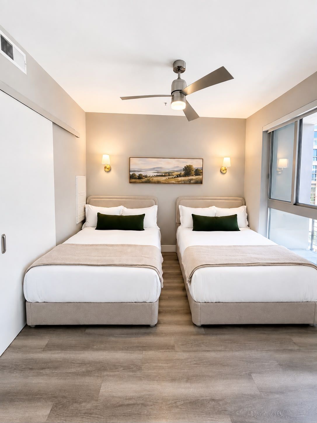Une chambre d’hôtel avec deux lits, un ventilateur de plafond, un tableau au mur et une fenêtre donnant sur un paysage.