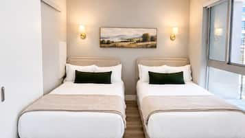 Une chambre d’hôtel avec deux lits, un ventilateur de plafond, un tableau au mur et une fenêtre donnant sur un paysage.