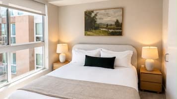Habitación de hotel con una cama grande, dos lámparas de noche, un ventilador de techo y una ventana con vistas a la ciudad.