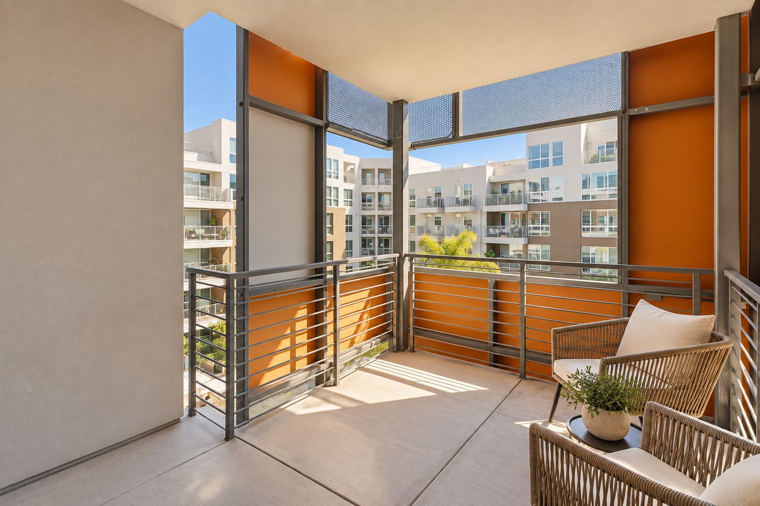 A balcony with a view of neighboring buildings, a wicker chair, and a potted plant.