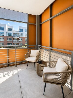 A balcony with two wicker chairs and a small round table, overlooking a building with multiple windows.