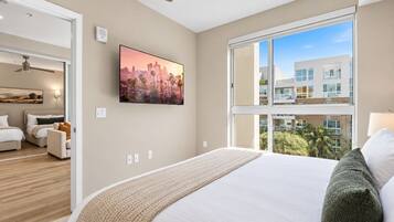 A modern hotel room with a large bed, a cityscape painting, and a view of a building through the window.