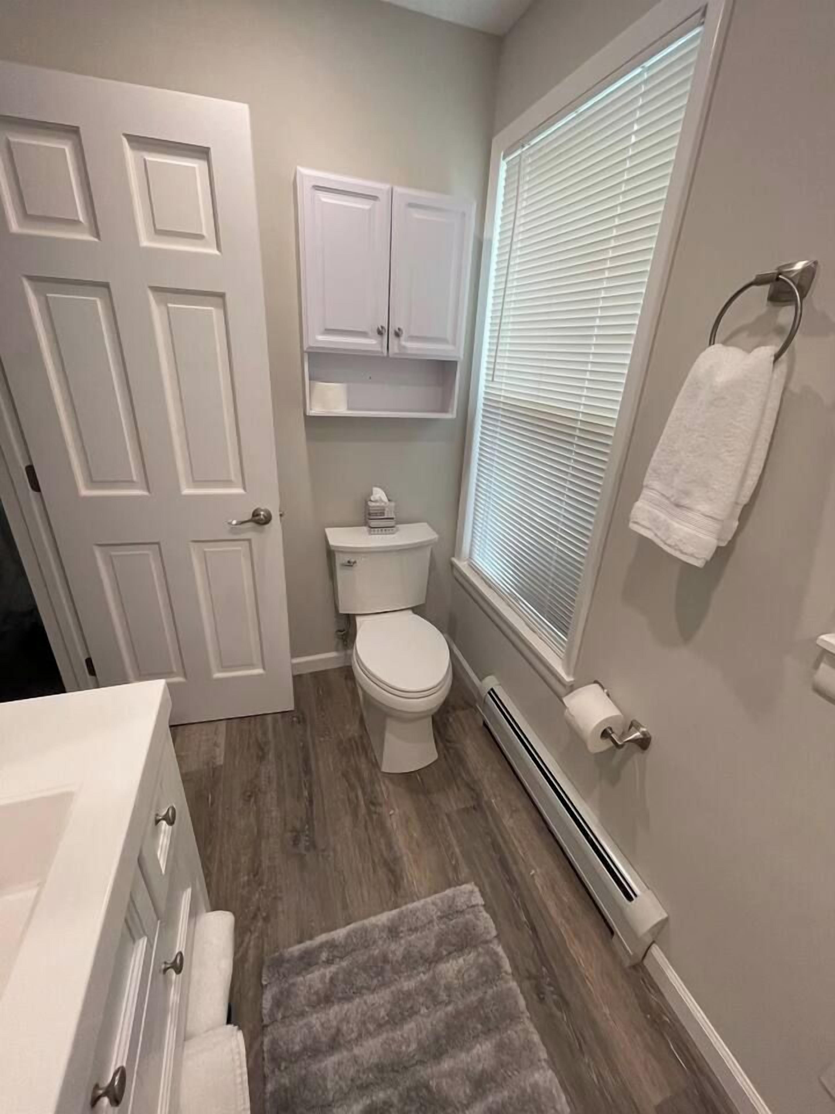 Un baño con inodoro, un armario blanco, toallero y una ventana con persianas.
