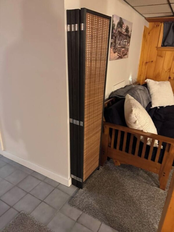 Une pièce comprenant un lit, une tête de lit en bois, une étagère fixée au mur et un petit tapis.