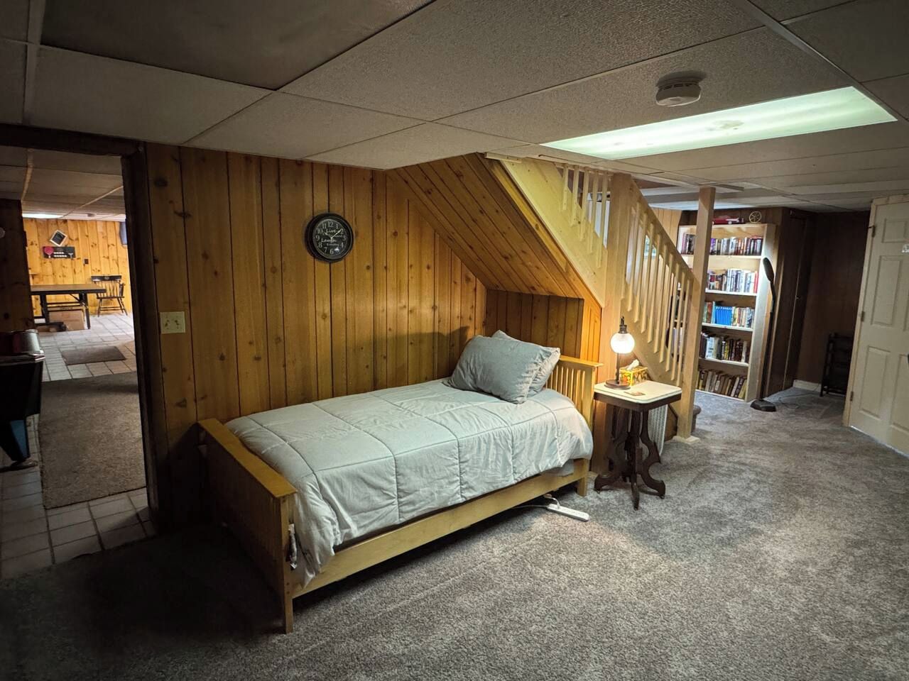 Una camera da letto con un letto in legno, un comodino con una lampada, una scala e una libreria sullo sfondo.
