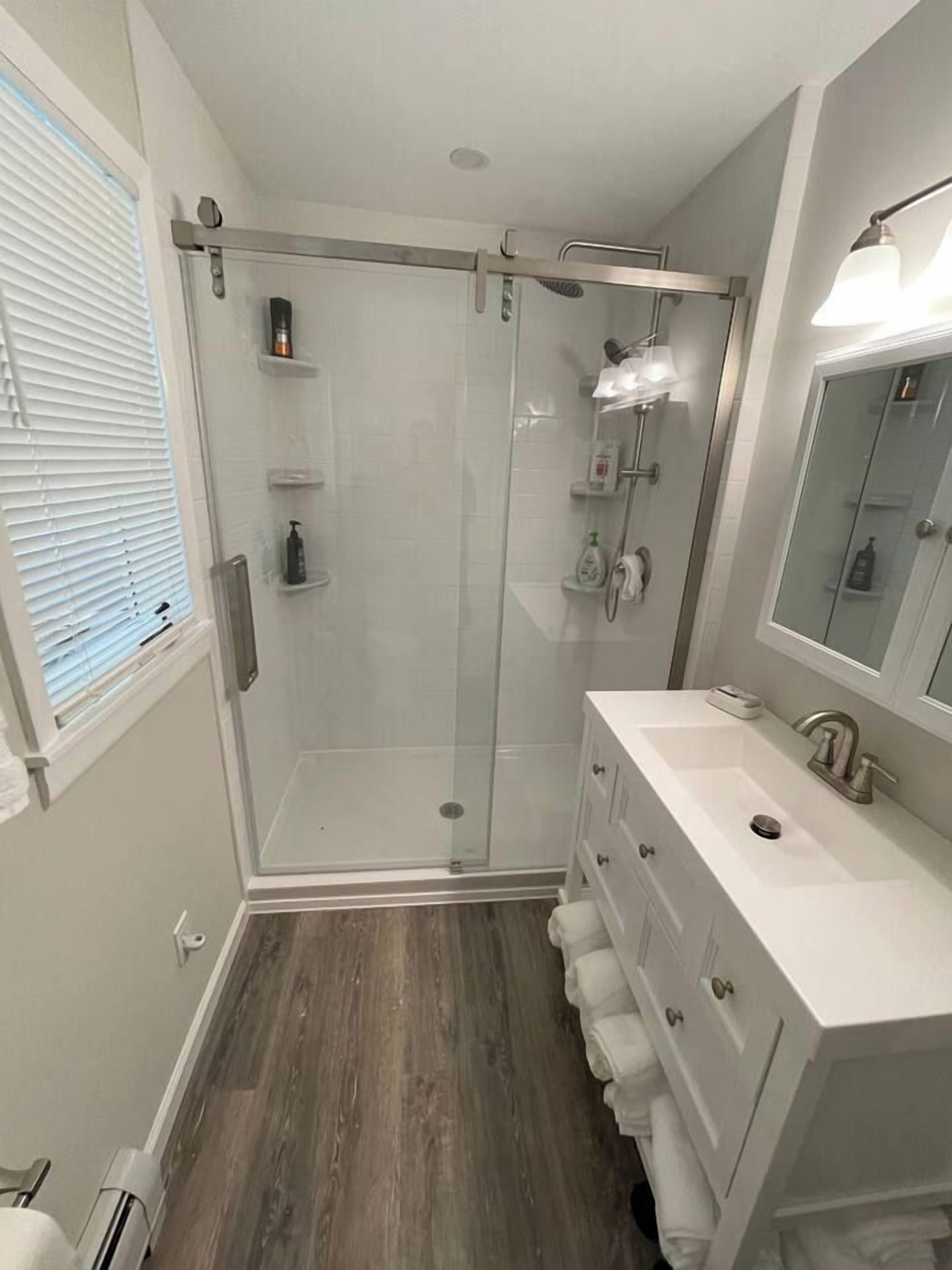 Een moderne badkamer met een douchecabine van glas, een wit wastafelmeubel met spiegel en een houten vloer.