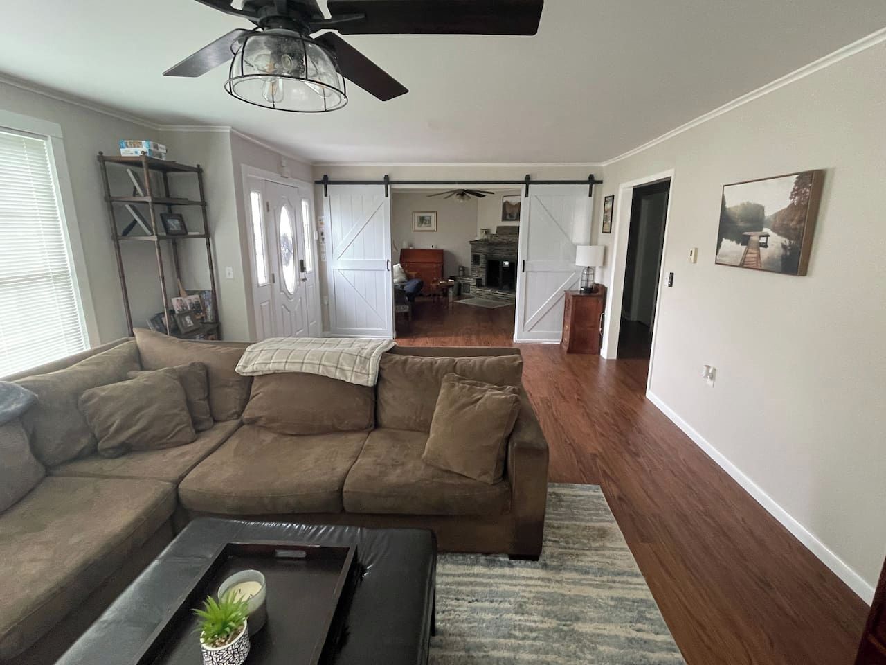A living room with a sectional sofa, a coffee table with a plant, a ceiling fan, and a fireplace in the background.