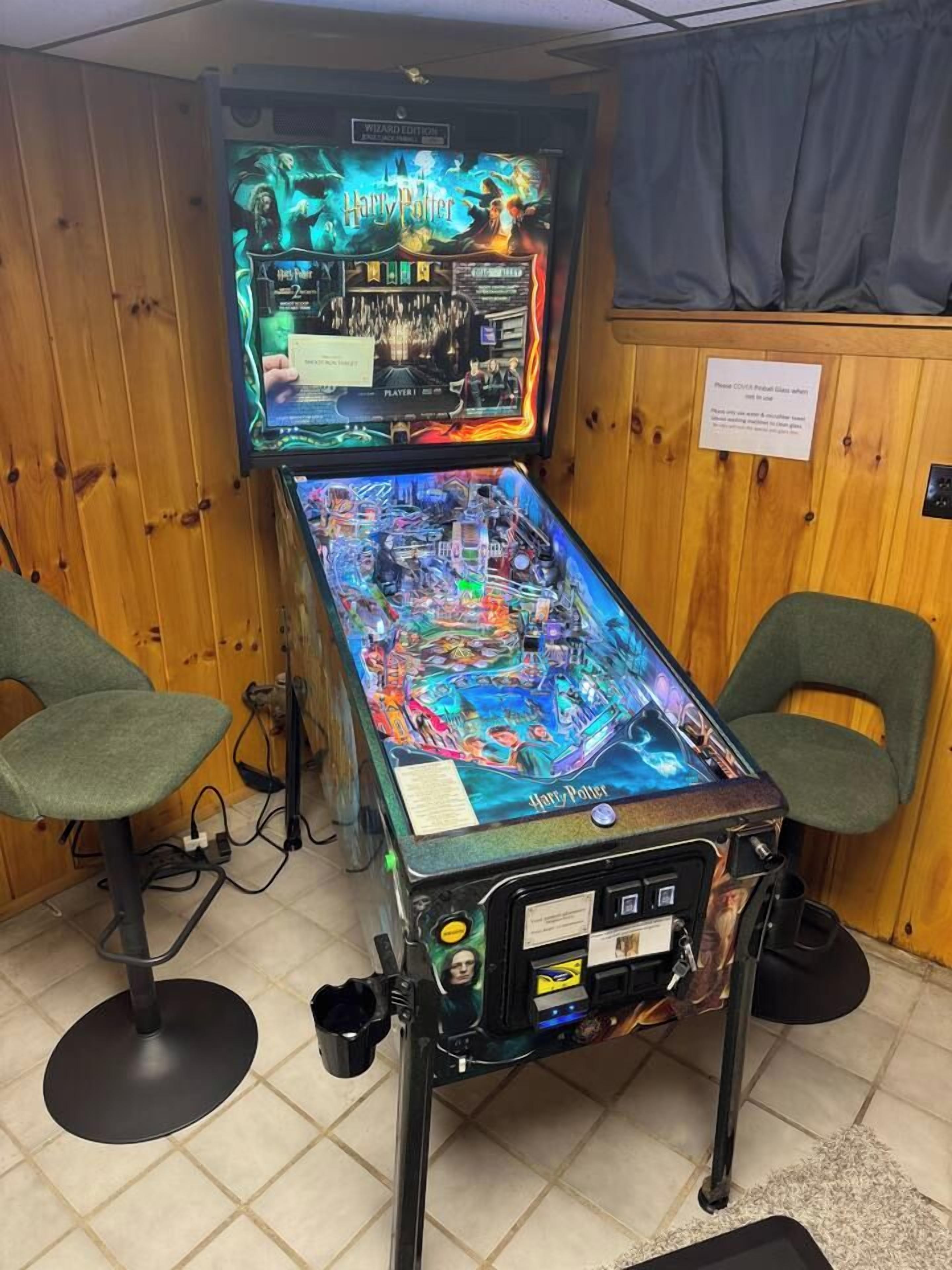 A pinball machine with a Harry Potter theme, placed in a room with wooden walls and two chairs.