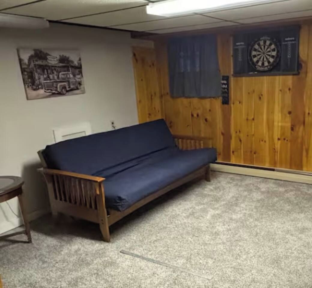 Una habitación con pared de madera, un sofá azul, un dardo y un cartel.