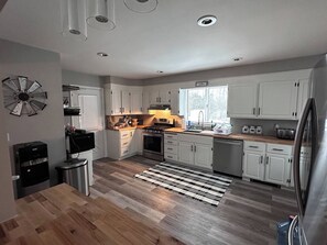 A modern kitchen with white cabinets, a stainless steel refrigerator, and a wooden floor.