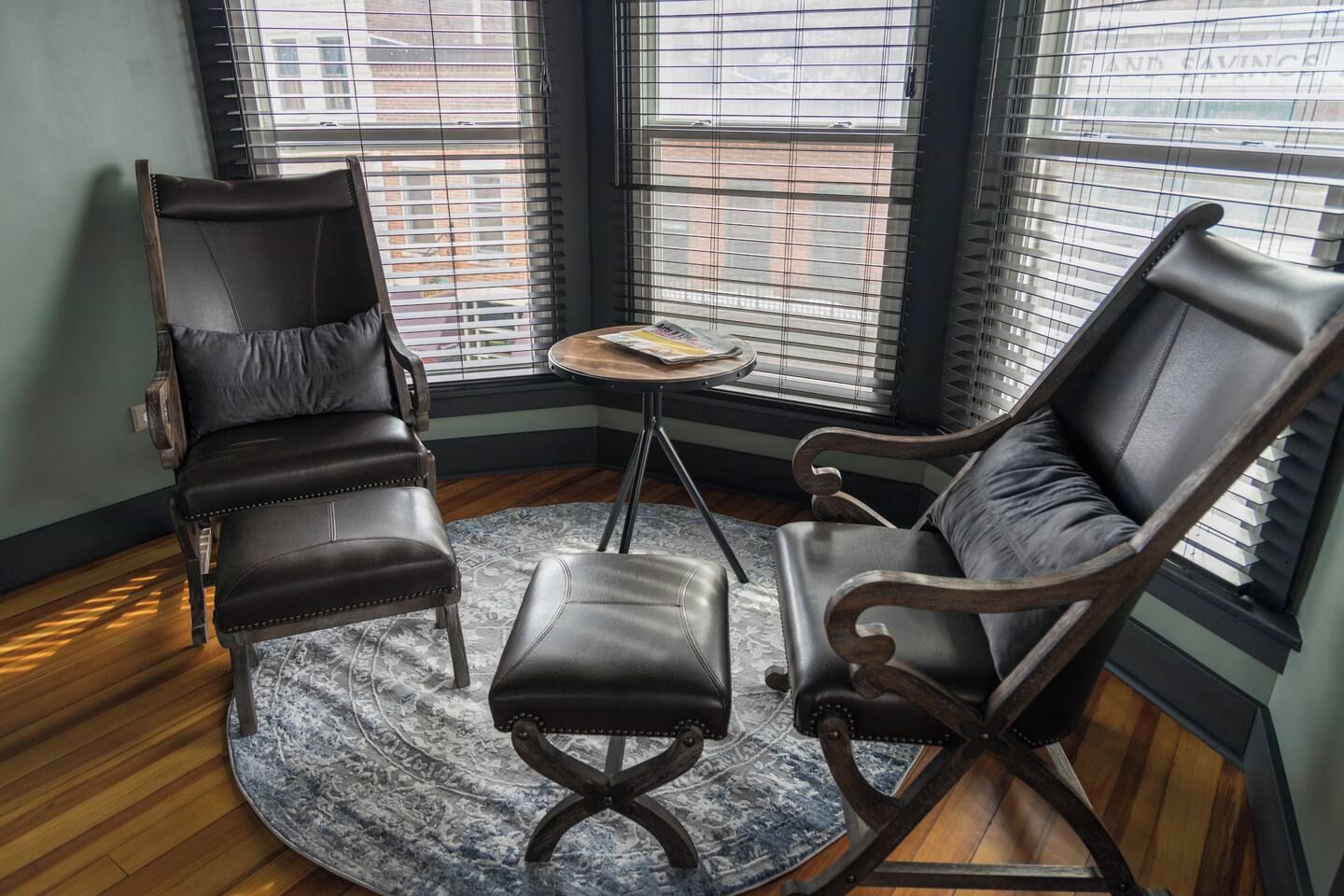 Ein Zimmer mit zwei Ledersesseln, einem kleinen runden Tisch und einem gemusterten Teppich.