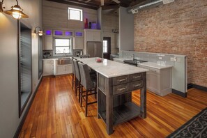 A modern kitchen with a central island, wooden flooring, and a brick accent wall.