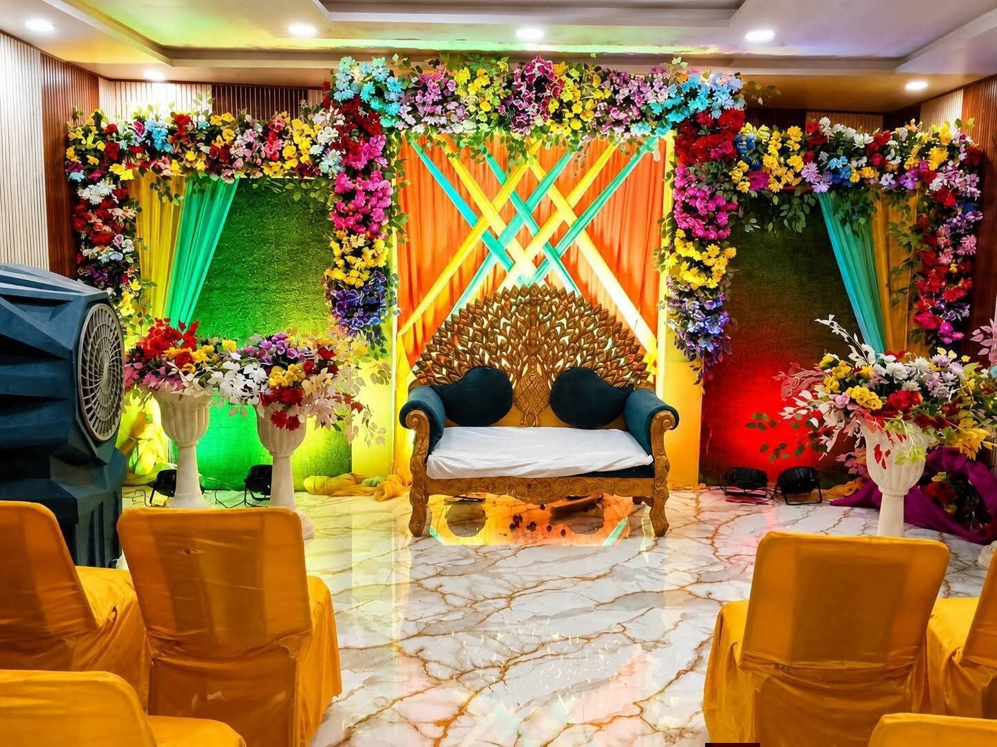 A room with a central bed, surrounded by chairs, and decorated with floral arrangements.
