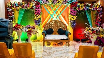 A room with a central bed, surrounded by chairs, and decorated with floral arrangements.
