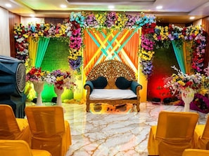 Una habitación con una cama central, rodeada de sillas y decorada con arreglos florales.
