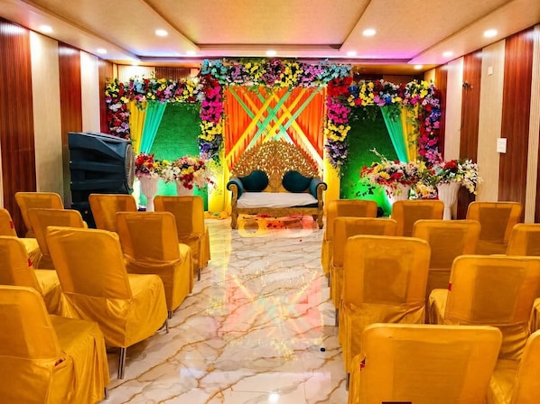 Un salón con filas de sillas, un escenario con una silla dorada y adornos florales.