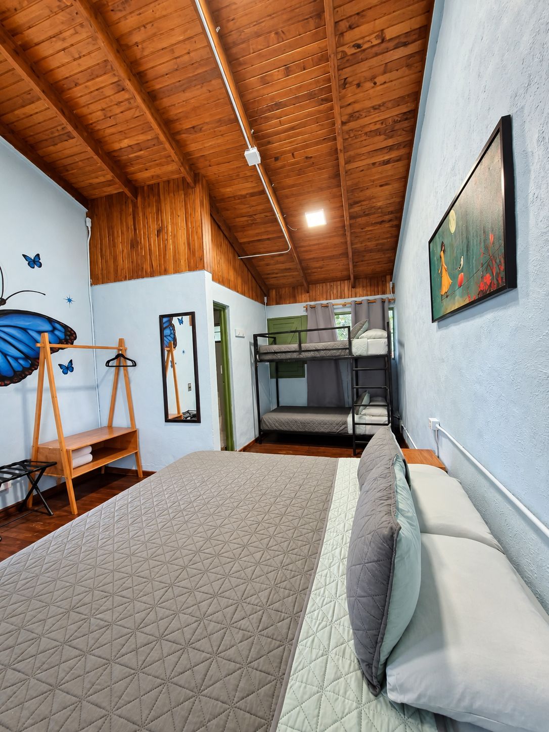 Une chambre avec un lit superposé, un lit simple, des poutres en bois au plafond, un tableau au mur et une décoration en forme de papillon.