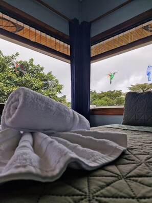 Een bed met een opgerolde handdoek, een gewatteerd kussen en uitzicht op de lucht met vogels.