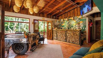 A rustic interior with a wooden ceiling, a vintage vehicle, a bar area with a mural, and a television.