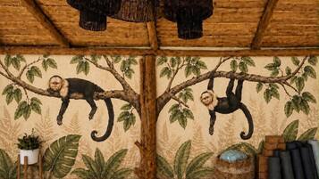 Una habitación con techo de madera, un mural de monos en un árbol, una pequeña planta y una cesta tejida.
