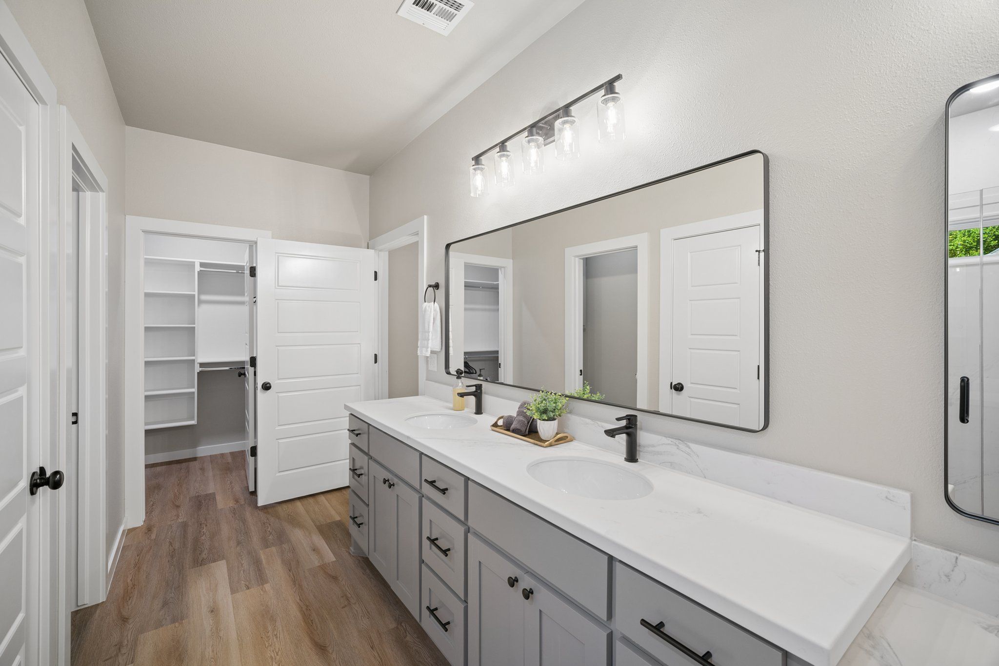 A modern bathroom with a double sink vanity, a large mirror, and a walk-in closet.
