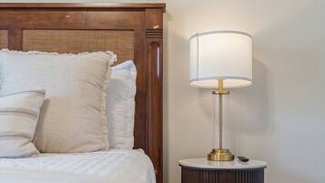 A neatly made bed with white linens and a headboard, a bedside lamp on a wooden nightstand, and a framed sign on the wall.