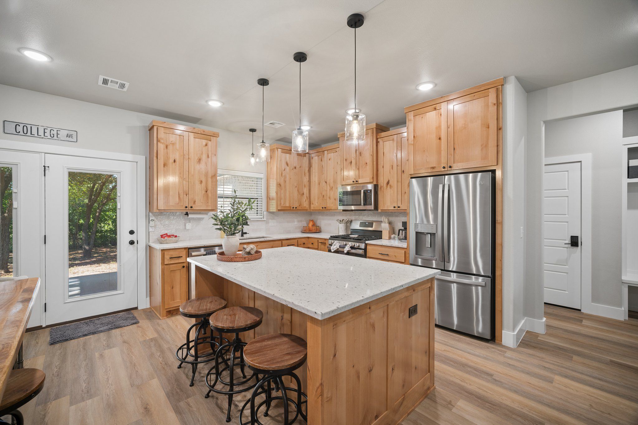 A modern kitchen with wooden cabinets, stainless steel appliances, and a central island with stools.