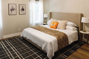 Ein Hotelzimmer mit einem großen Bett, einem gemusterten Teppich, zwei Wandleuchten und zwei gerahmten Bildern.