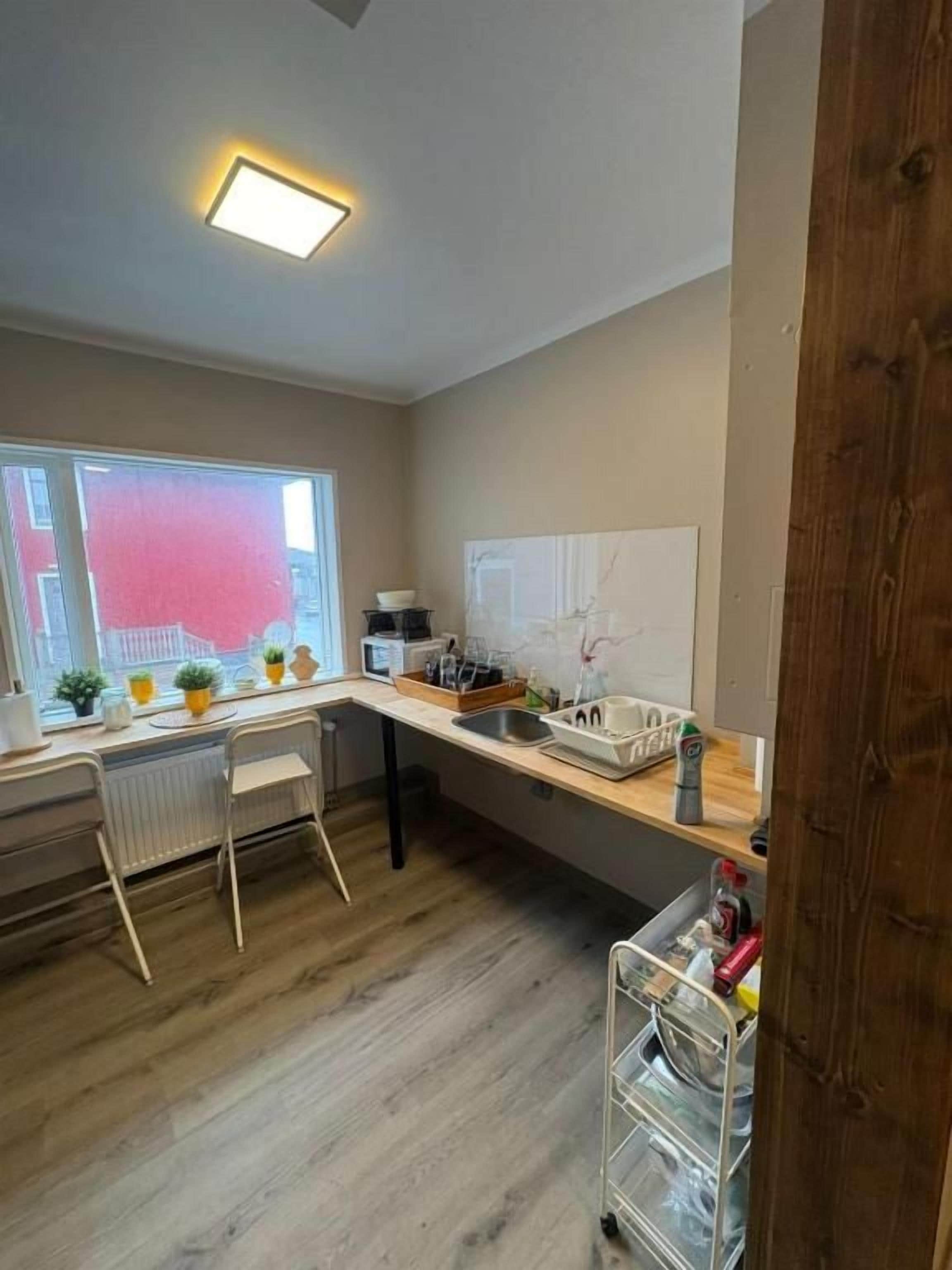Cozinha com bancada de madeira, radiador branco e janela com vista para um prédio vermelho.