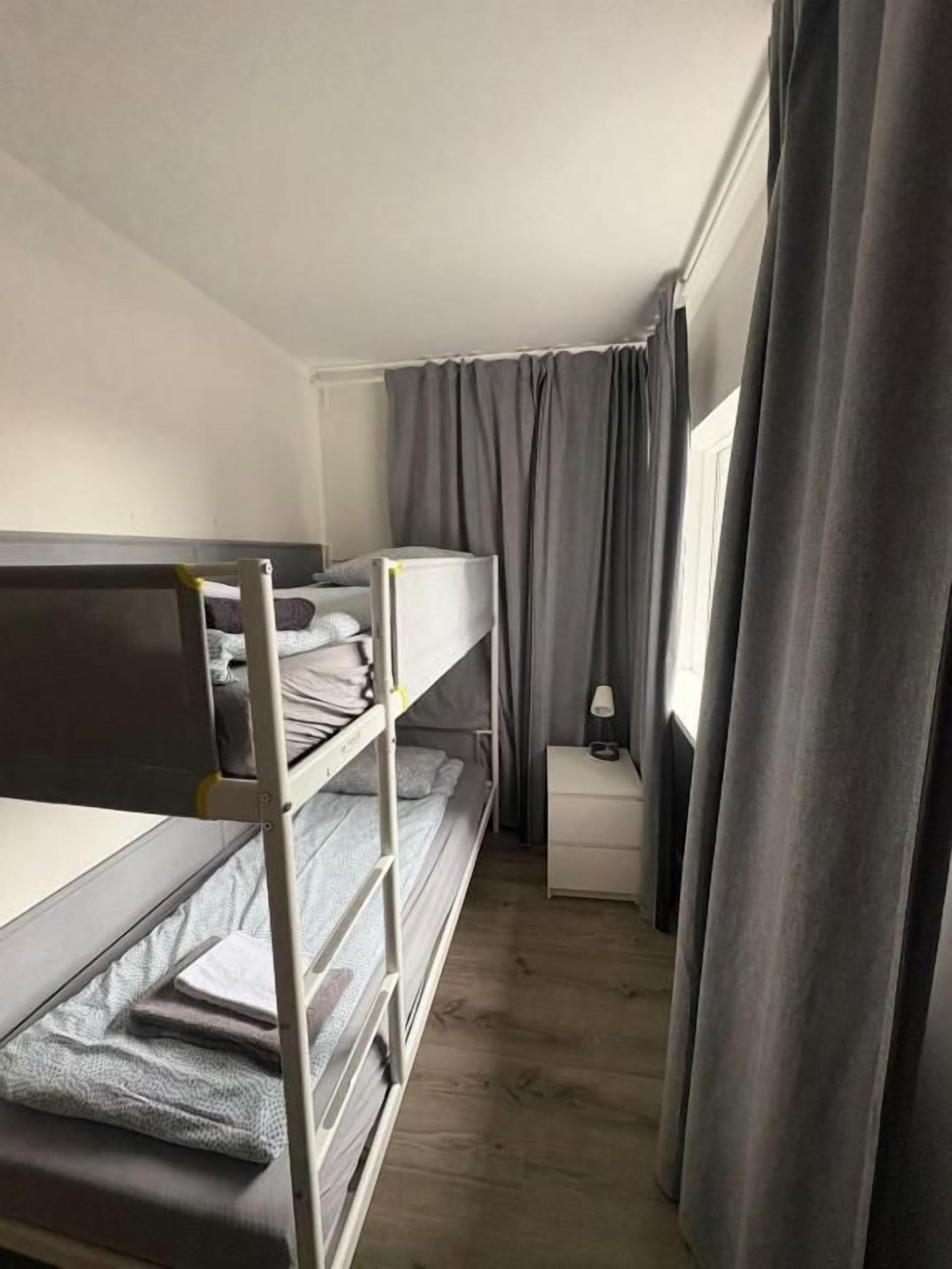 Una habitación con literas, una mesita de noche, una lámpara y una ventana con cortinas.