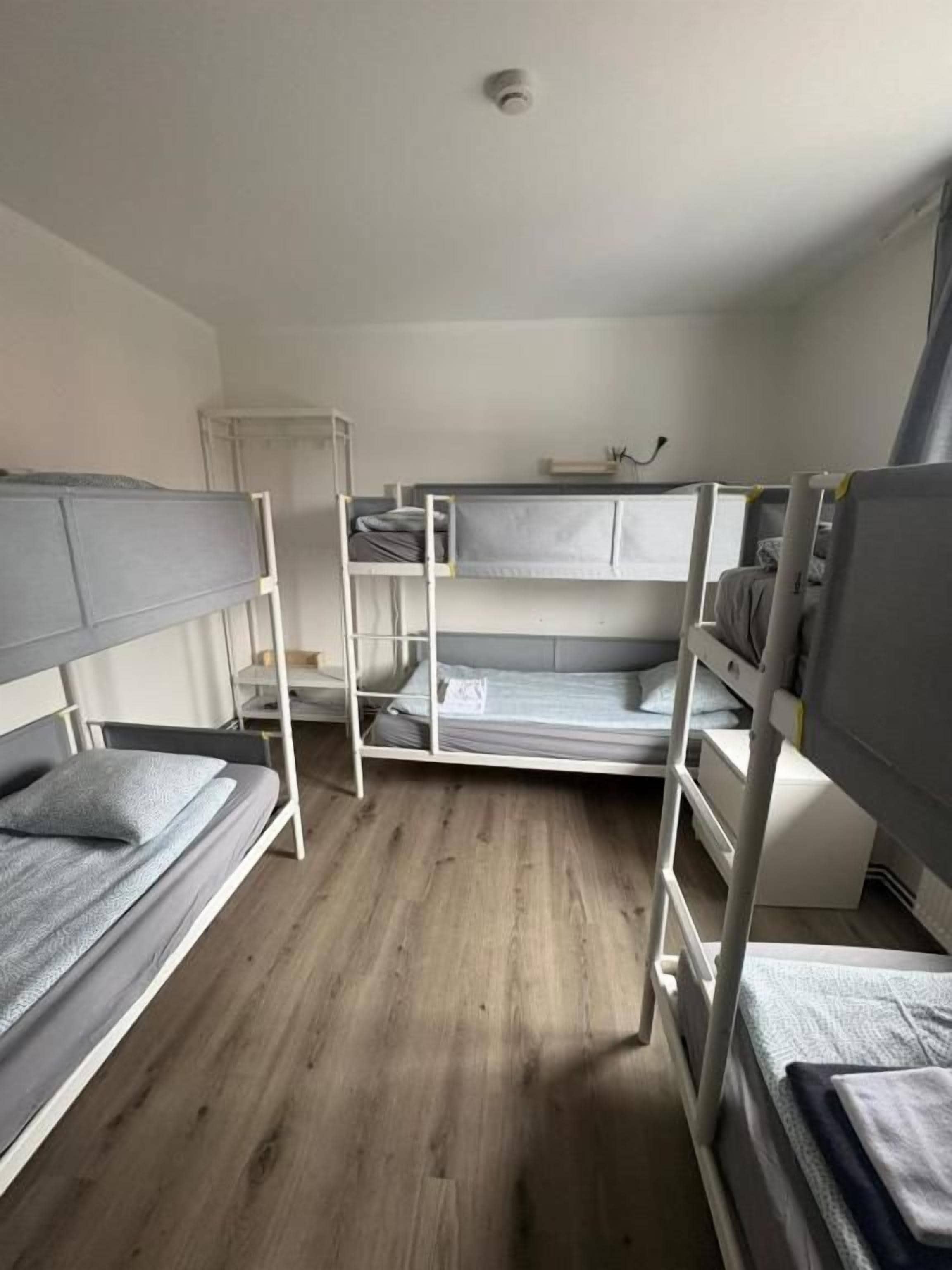Habitación con literas, suelo de madera, techo blanco y un pequeño armario blanco.