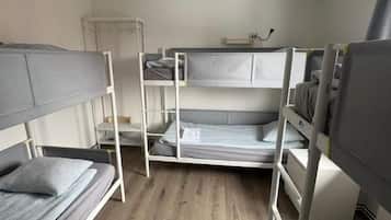 Habitación con literas, suelo de madera, techo blanco y un pequeño armario blanco.