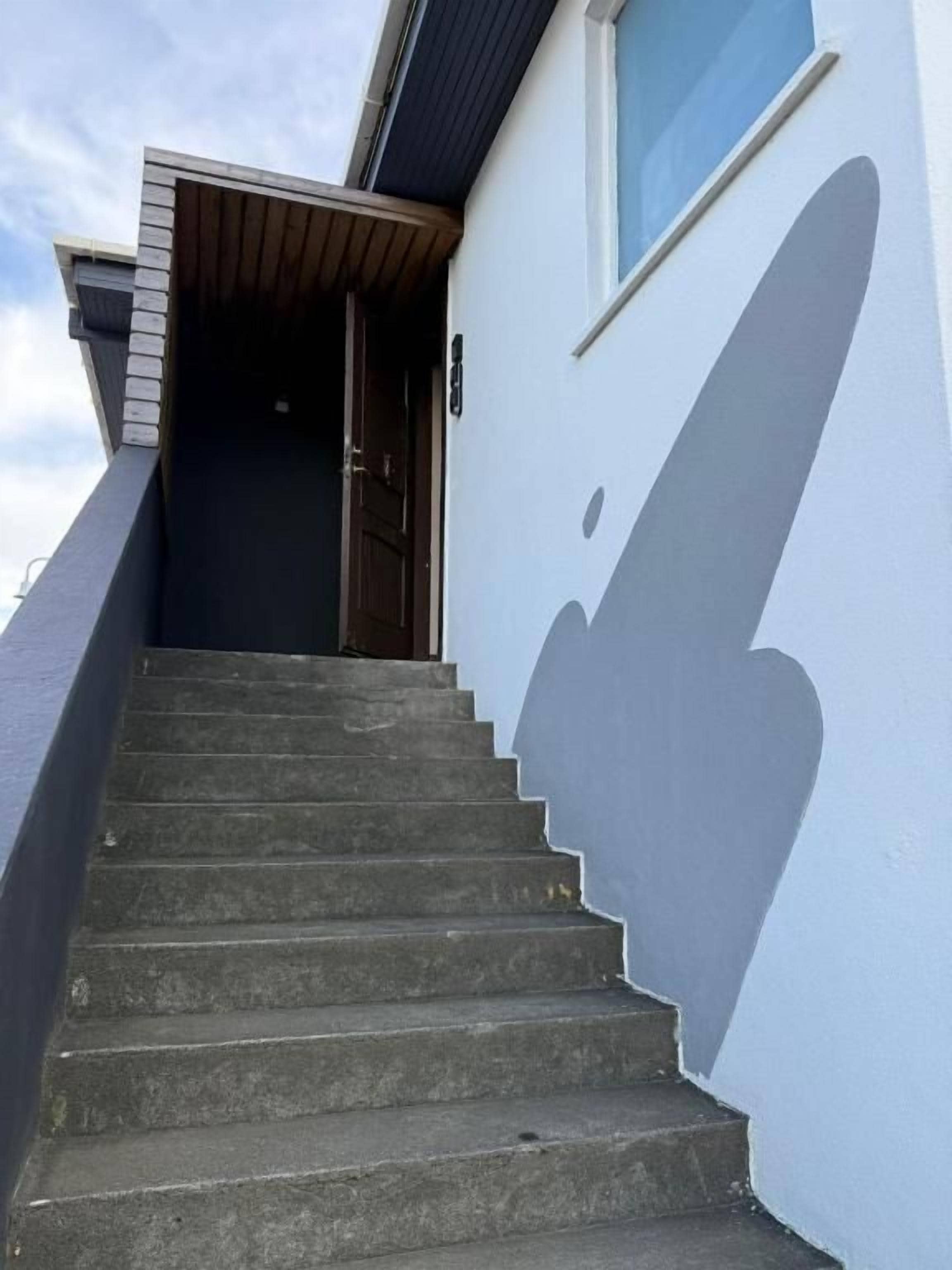 Una escalera que lleva a una puerta, con una sombra en la pared.