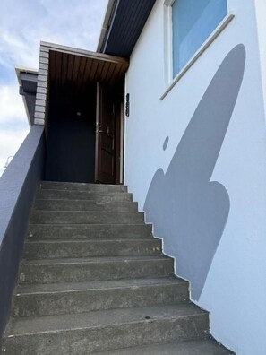 Eine Treppe führt zu einer Tür, an deren Wand ein Schatten fällt.