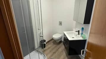 Ein kleines Badezimmer mit Glasdusche, Toilette, Waschbecken mit Spiegel und einem kleinen Schrank.