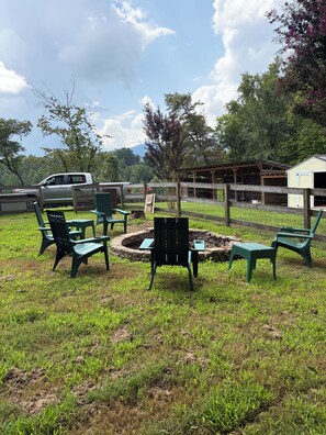 Ein Sitzbereich im Freien mit Stühlen und einem Feuerkorb, umgeben von einem Holzzaun und einer Wiese.