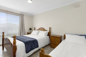 Un dormitori amb llit de fusta, una taula de nit i una finestra amb cortines.