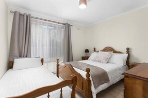 A hotel room with two beds, a wooden headboard, a bedside table with a lamp, and a window with curtains. - The Moorings Tides & Tails - Pets Welcome! (St Leonards)