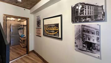 Un pasillo con fotografías históricas enmarcadas en la pared, un refrigerador antiguo y una escalera de madera.