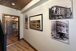 A hallway with framed historical photographs on the wall, a vintage refrigerator, and a wooden staircase.